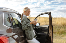Woman by a car looking at her phone after a vehicle accident on vacation